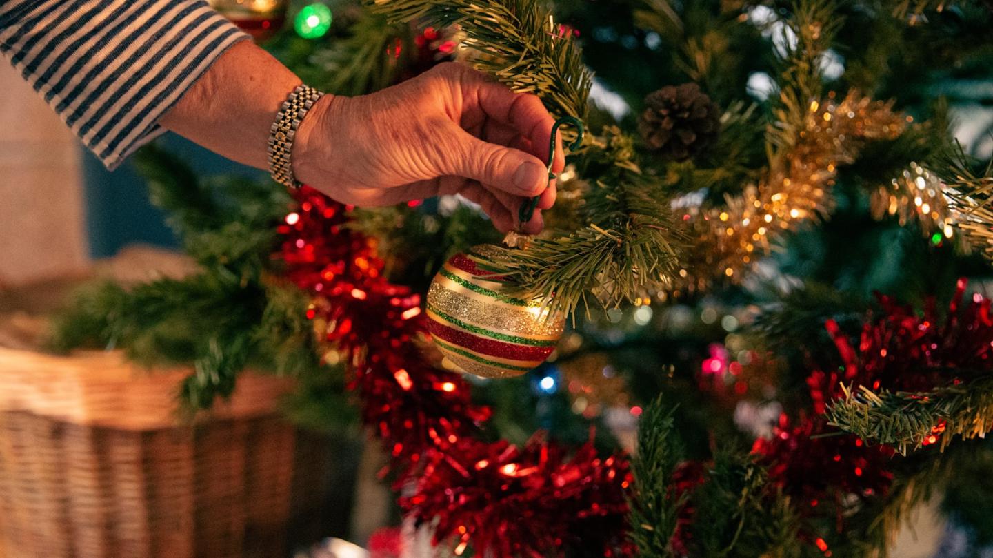 Close up image of hand placing bauble on a Christmas tree indoors
