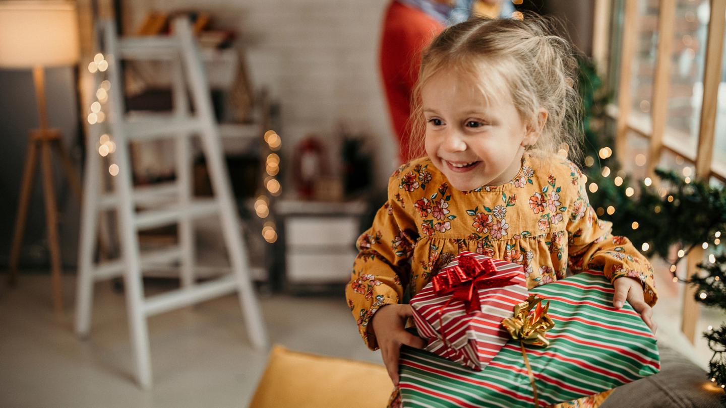 Excited young girl carrying presents from the Christmas tree